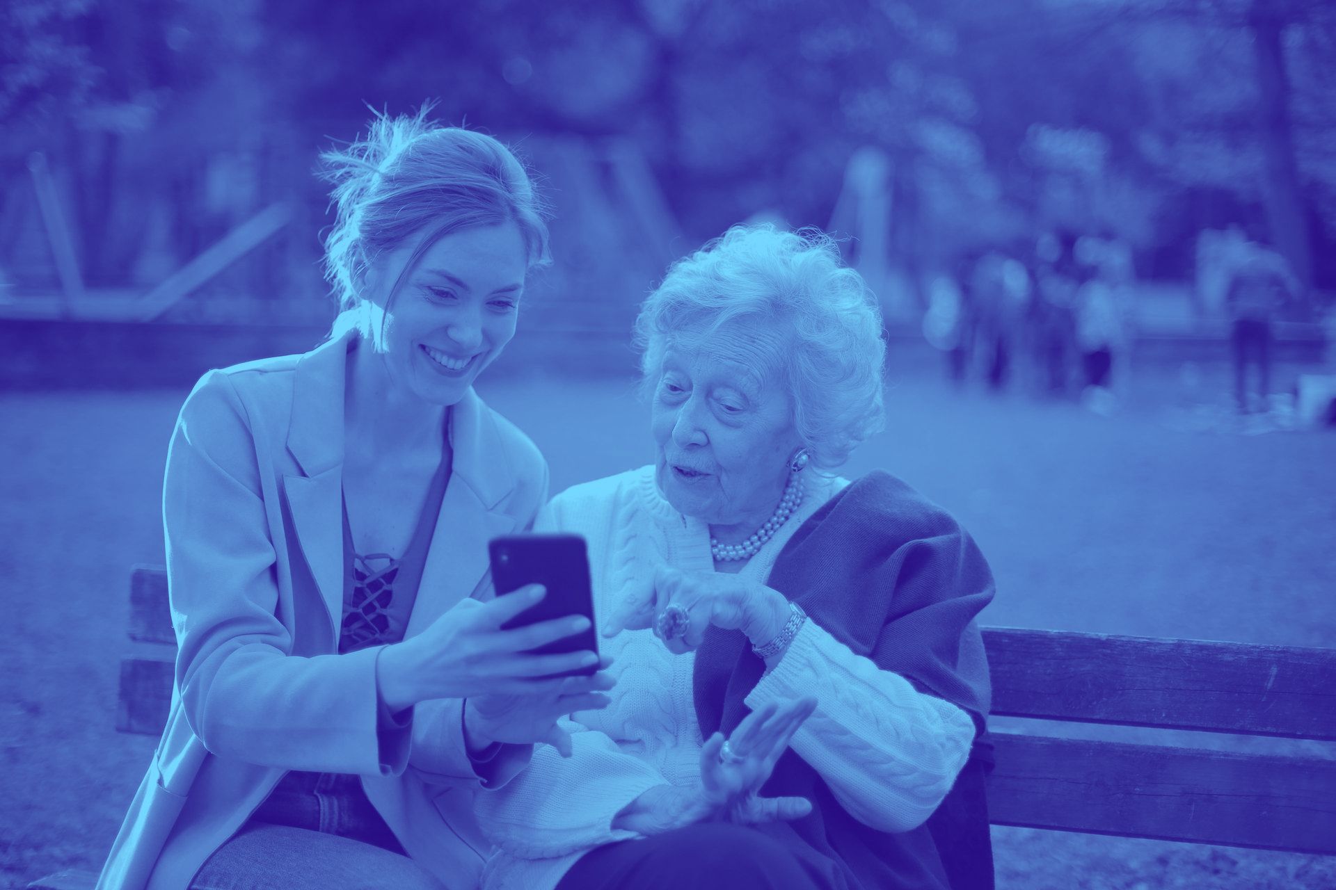 Two women are sitting on a bench looking at a cell phone.