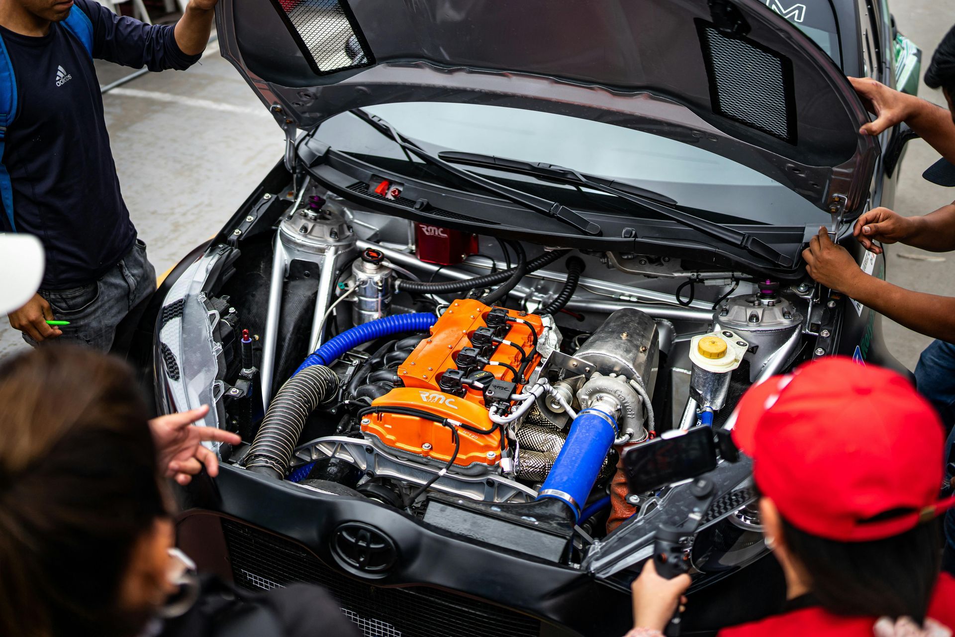 A group of people are looking under the hood of a car.