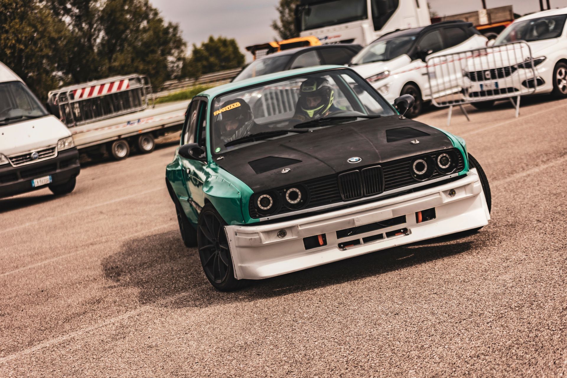 A green and black race car is driving down a road in a parking lot.