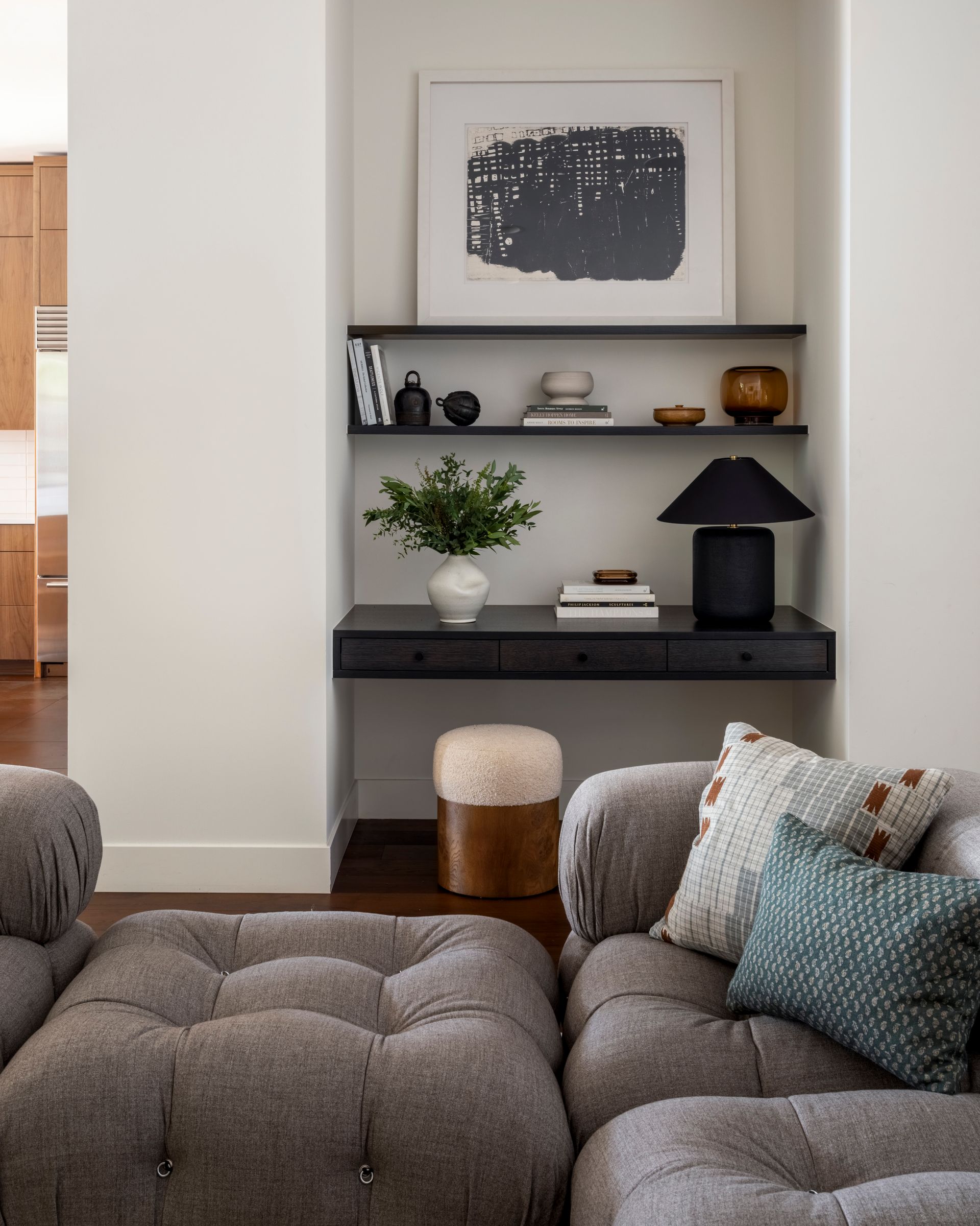 Built-in desk with shelves, art, and decor in a neutral-toned living area. Gray sectional and ottoman.