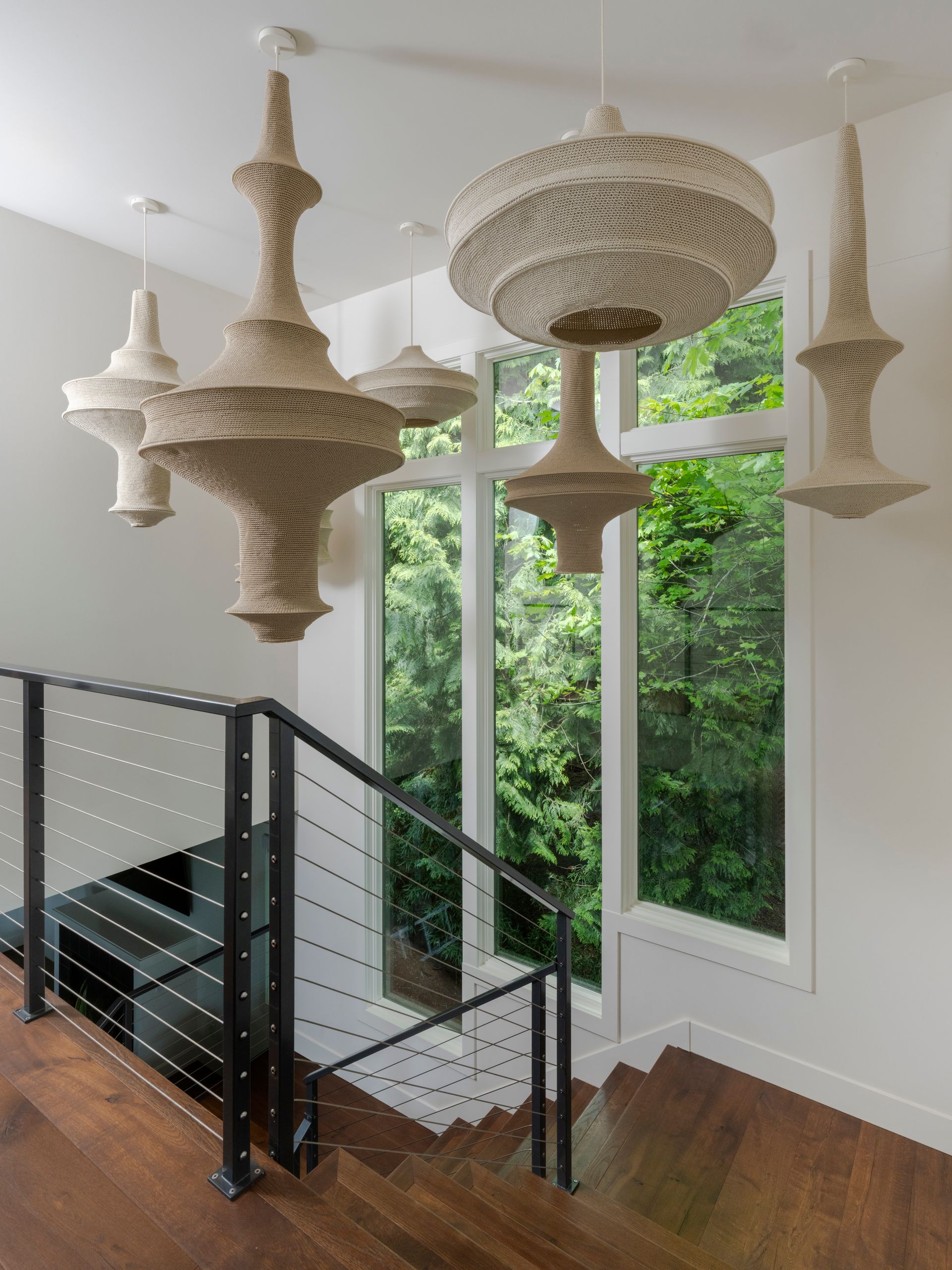 Ornate, beige chandeliers hanging in a stairwell with a large window overlooking trees.