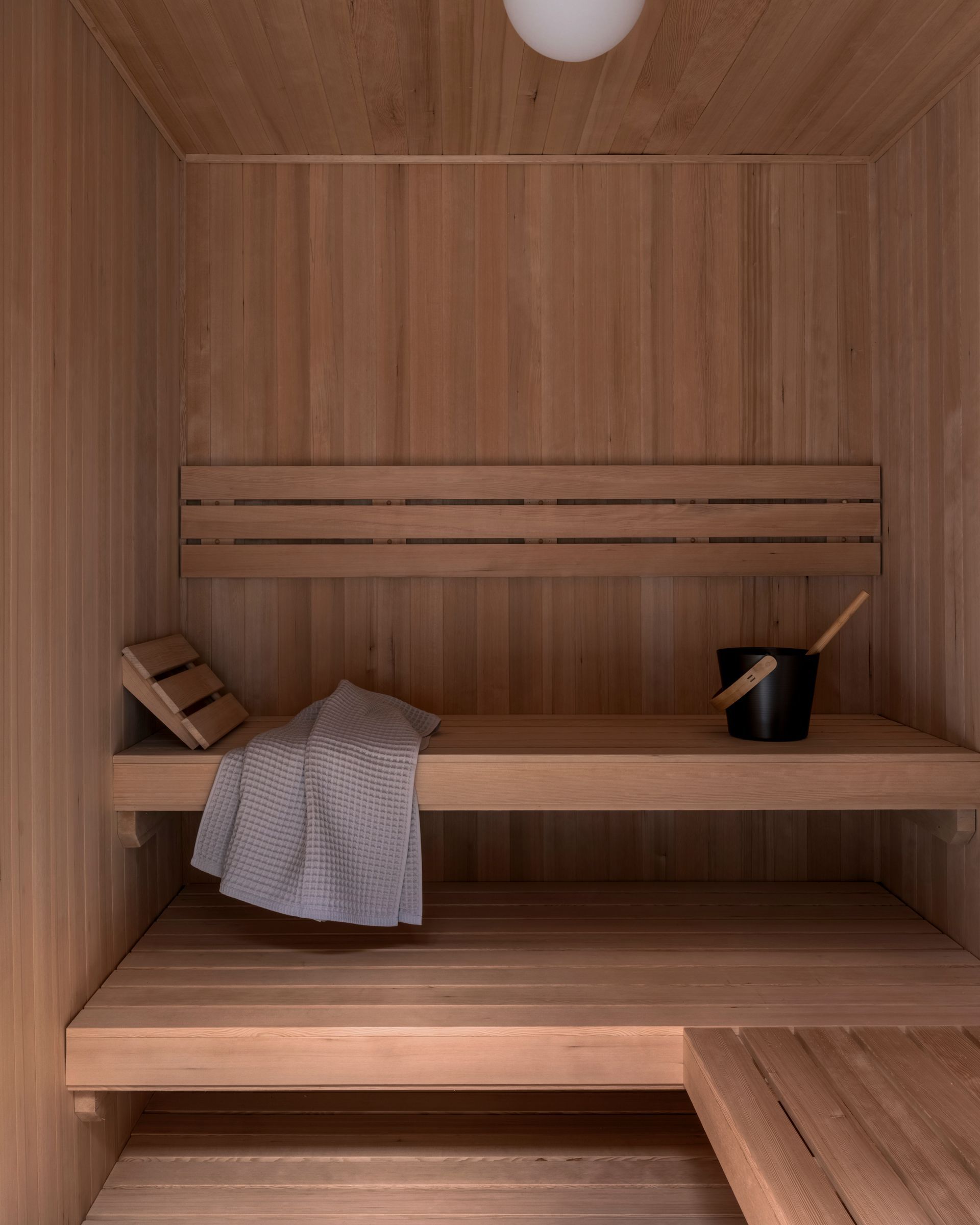 Wooden sauna interior with benches, towel, bucket, and ladle.