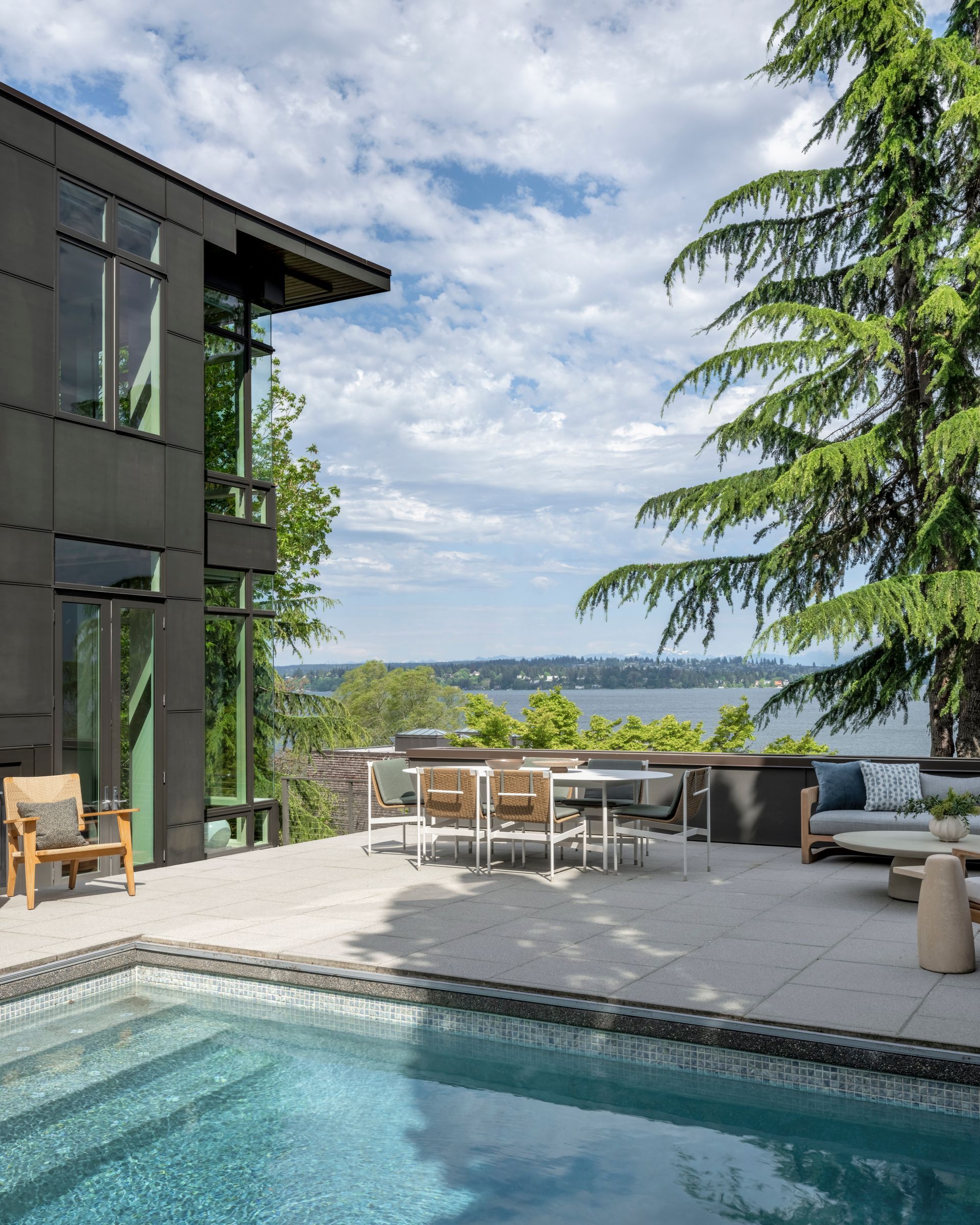 Modern home exterior with pool, patio furniture, and water view.