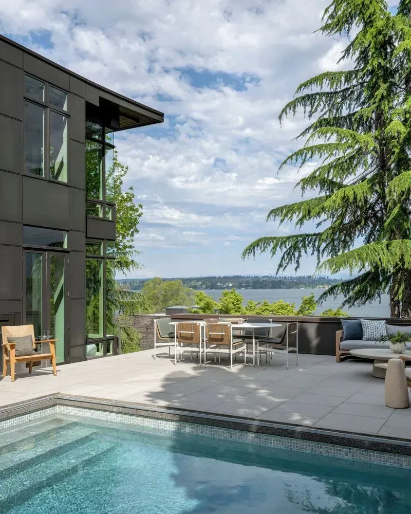 Modern home exterior with pool, patio furniture, and water view.