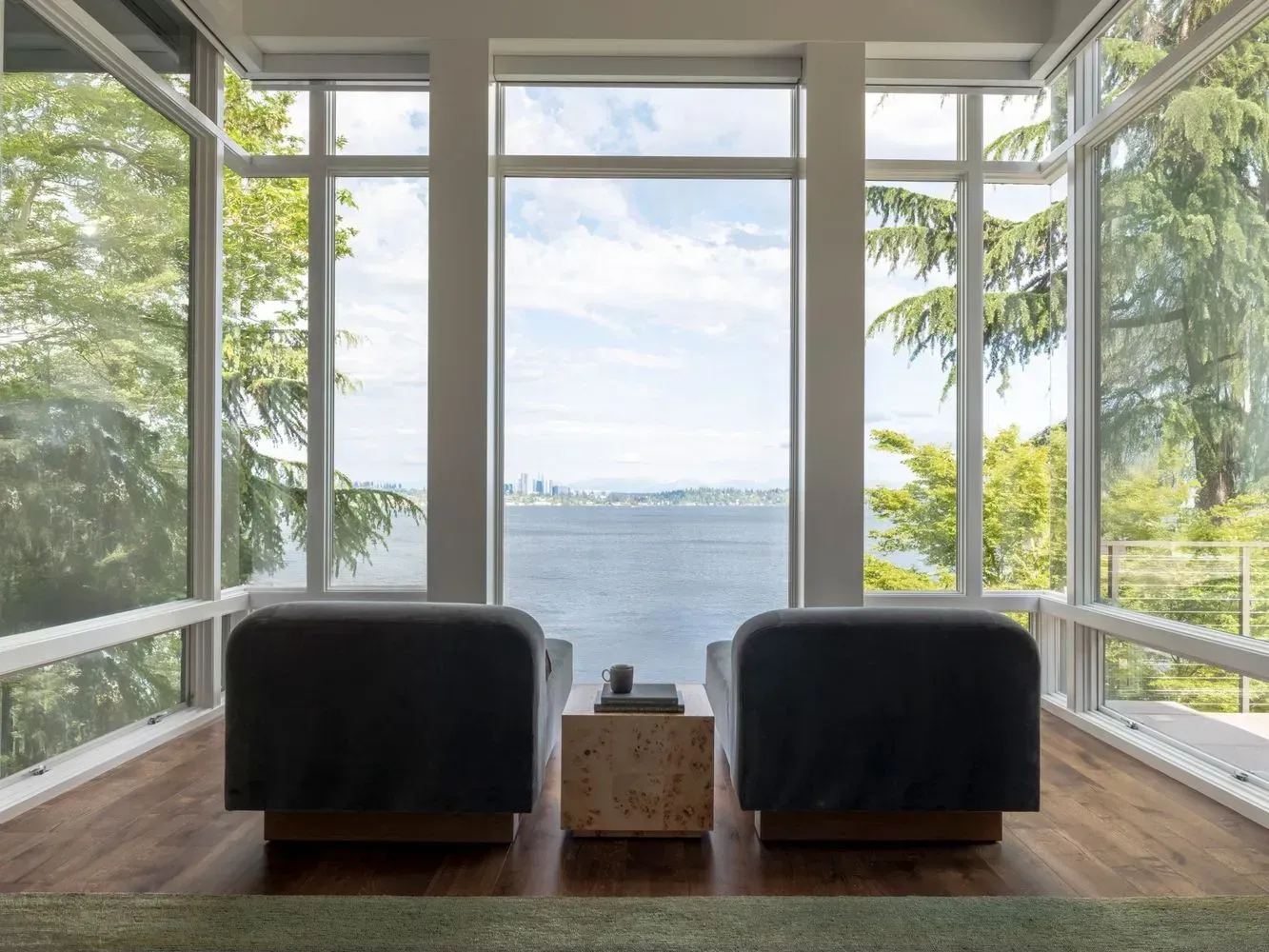 Two chairs face large windows with a view of a city skyline over water.