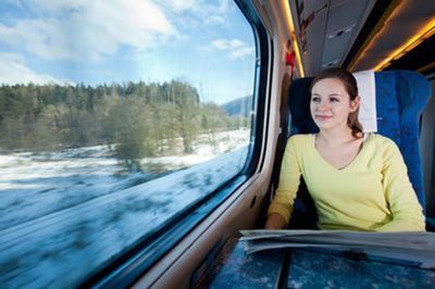 Passenger sitting by a train window, looking out at a snowy landscape under a blue sky.