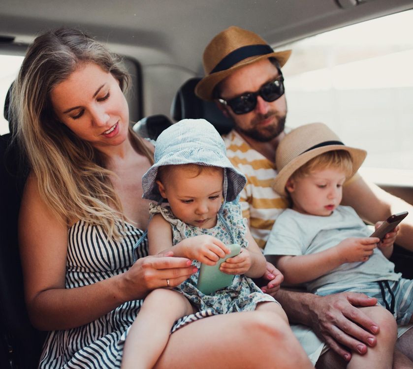 Family sitting together in a car, two children wearing hats and a man in sunglasses and a hat.