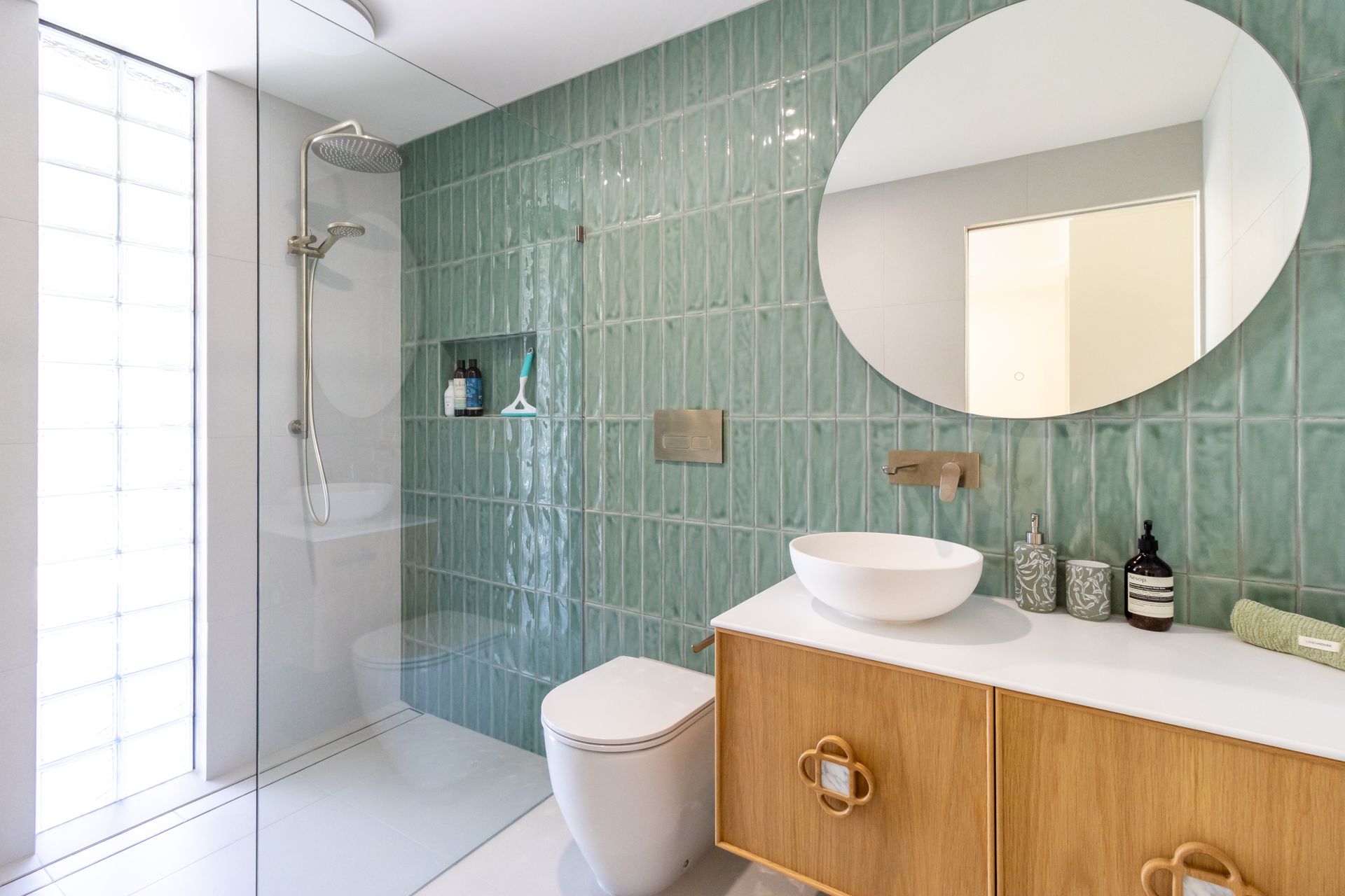 A bathroom with green tiles , a toilet , sink and shower.