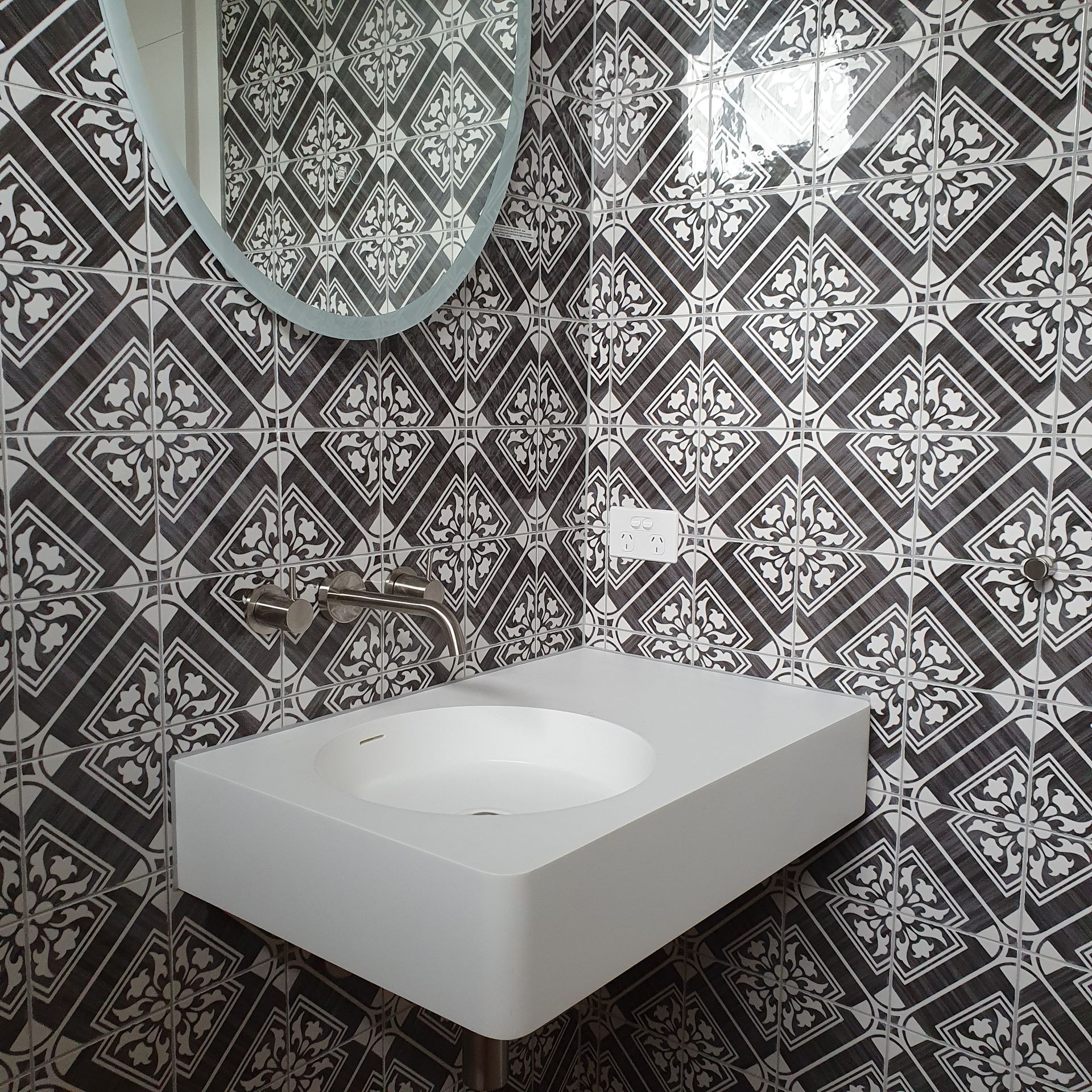 A bathroom with a sink , mirror and black and white tiles  | Building Services | Coastyle