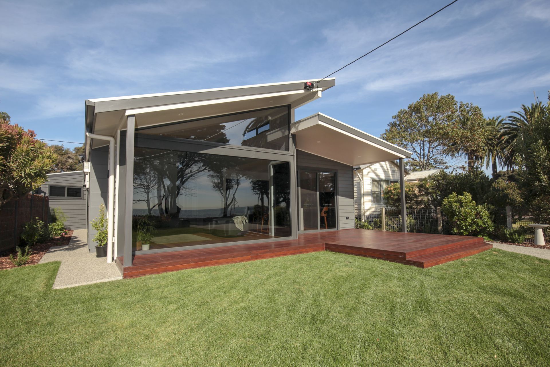 A house with a lot of windows is sitting on top of a lush green lawn.