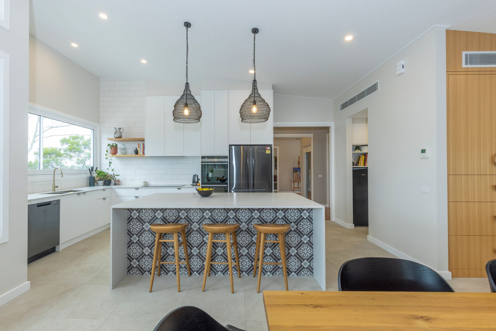 A kitchen with a large island , stools , a table and a refrigerator  | Building Services | Coastyle