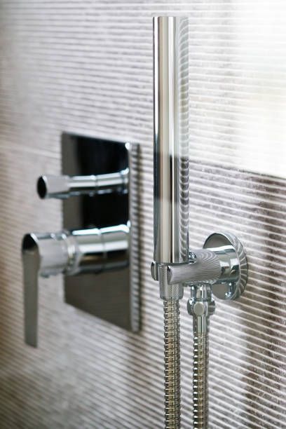 Shower faucet with two levers and a handheld shower on a tiled wall.