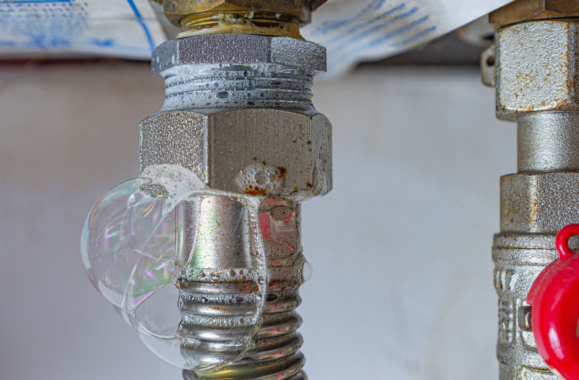 A metal gas pipe fitting with a large soap bubble, indicating a gas leak.