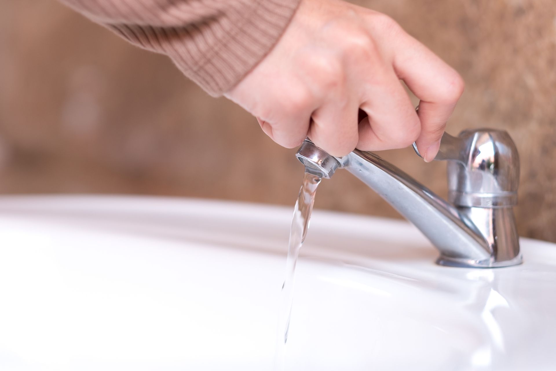 Hand turning on a chrome faucet over a white sink; water flows.