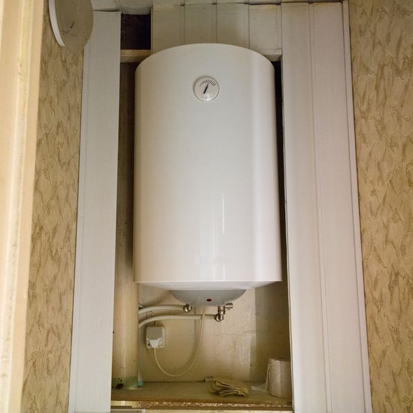 White water heater installed in a recessed wall space, with pipes and a temperature gauge visible.