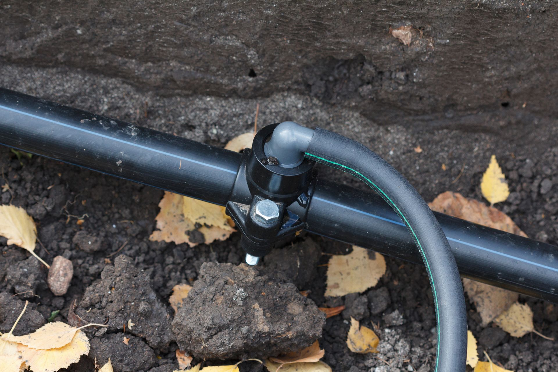 Black pipe with connected valve and tubing buried in dirt.