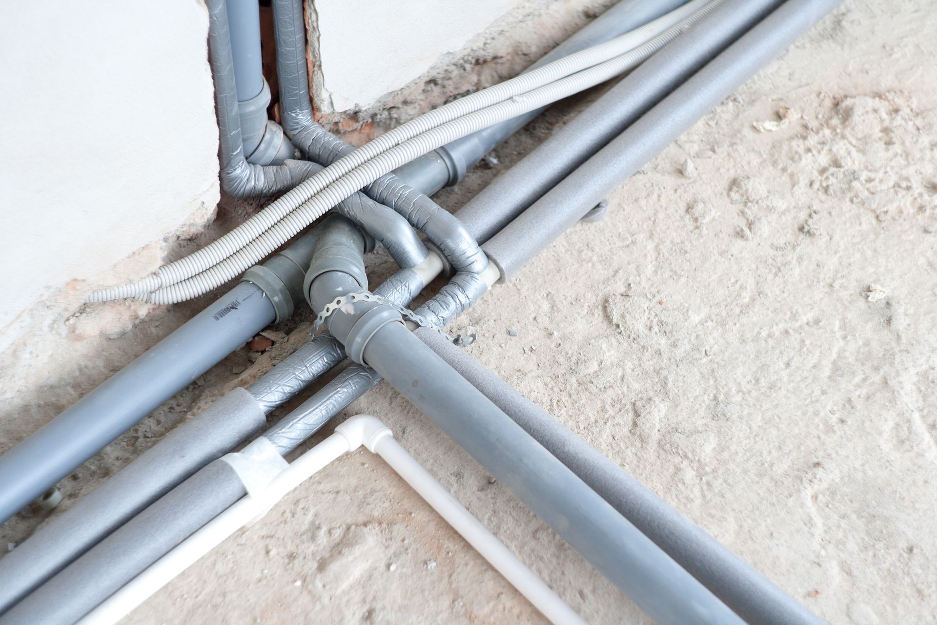 Gray PVC pipes and white cable wiring installed in a wall opening.