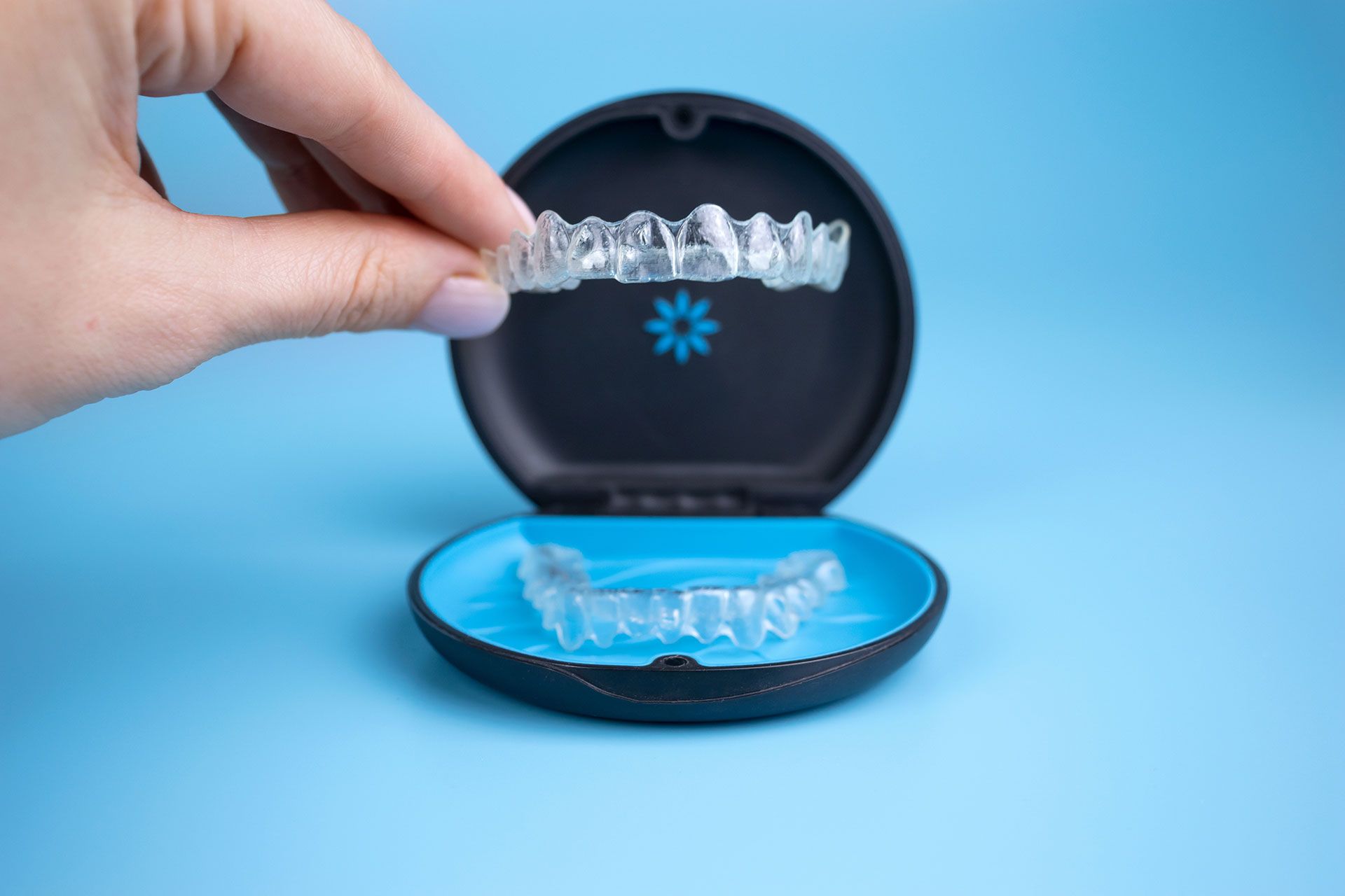 Woman holding invisalign transparent retainers with a box on the table, flatlay top view. Selective focus