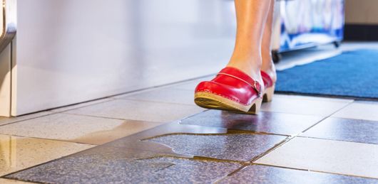A woman in New Jersey wearing red clogs is walking on a tiled floor that looks slippery and needs a slip preventive treatment.