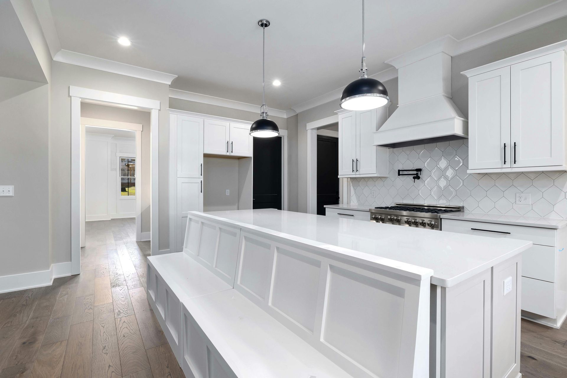 A kitchen with white cabinets , a large island , and a bench.