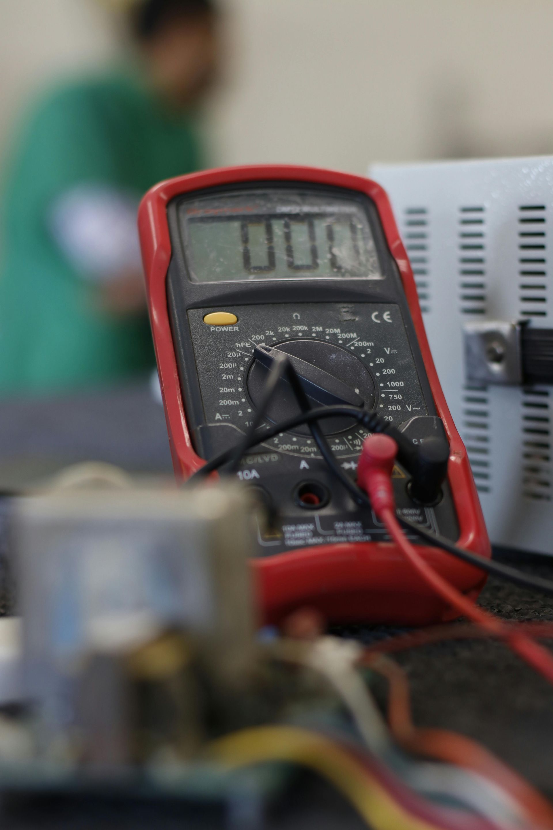 A red multimeter is sitting on a table next to some wires.