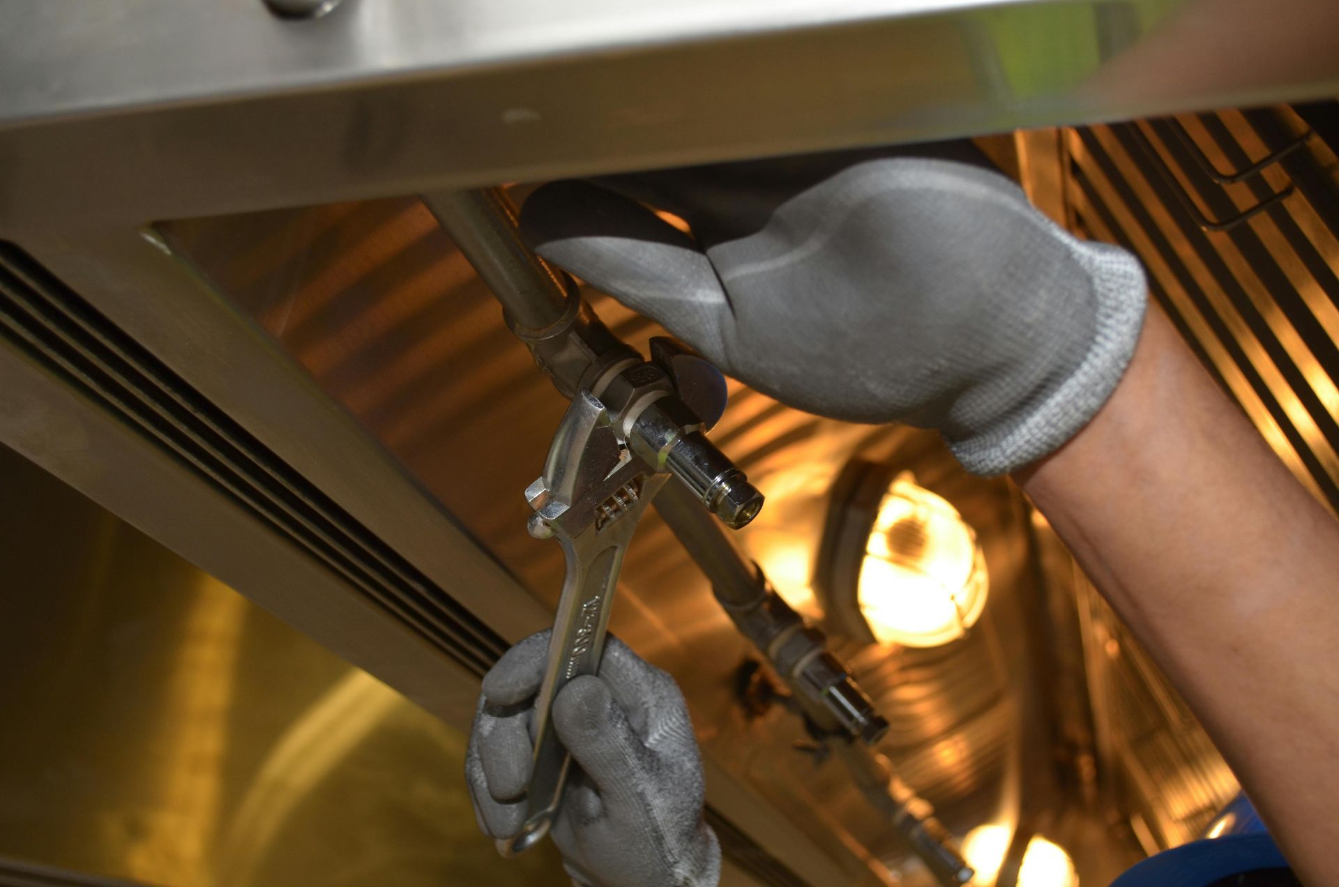 A person wearing gloves is working on a pipe with a wrench