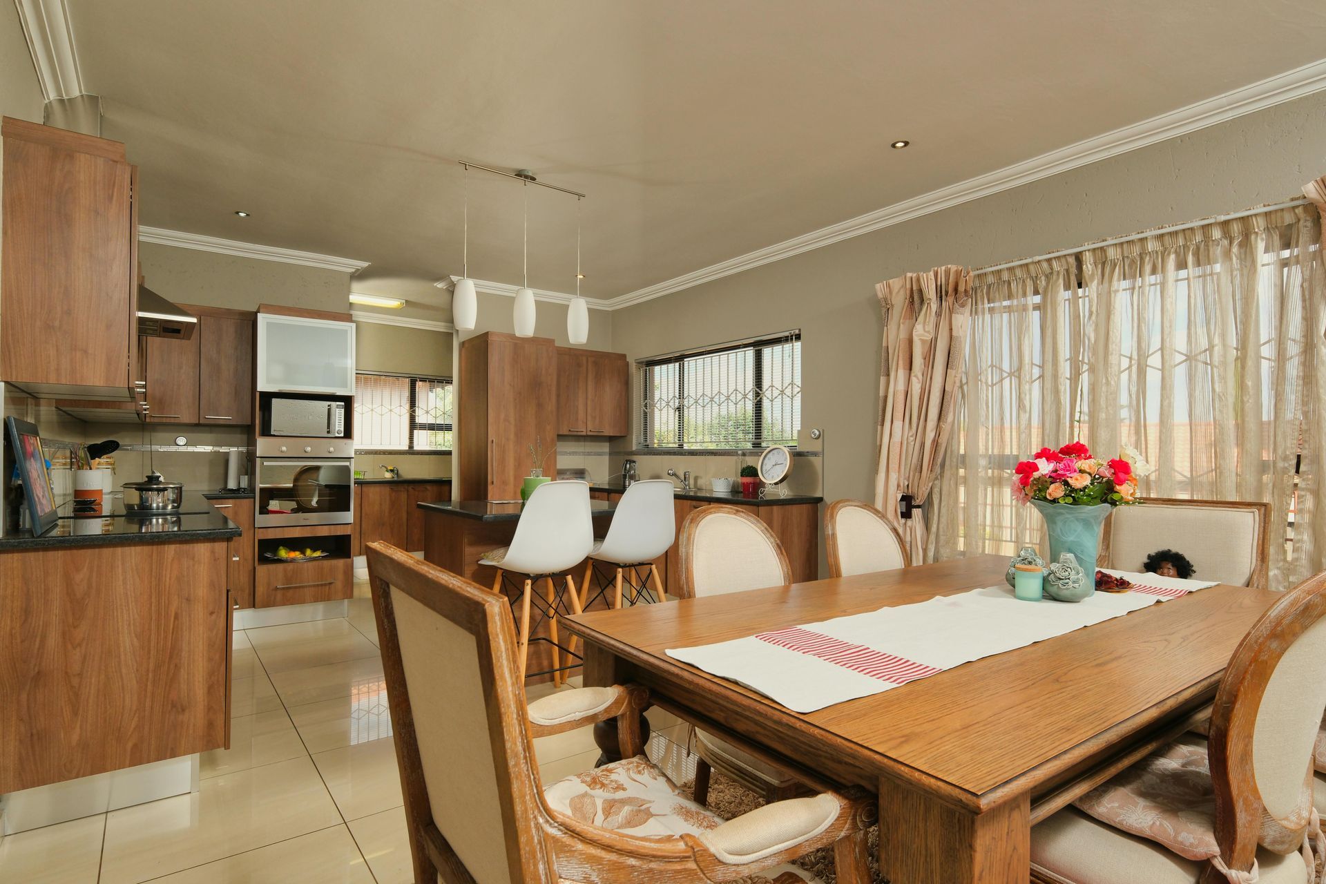 A dining room with a table and chairs and a kitchen in the background.