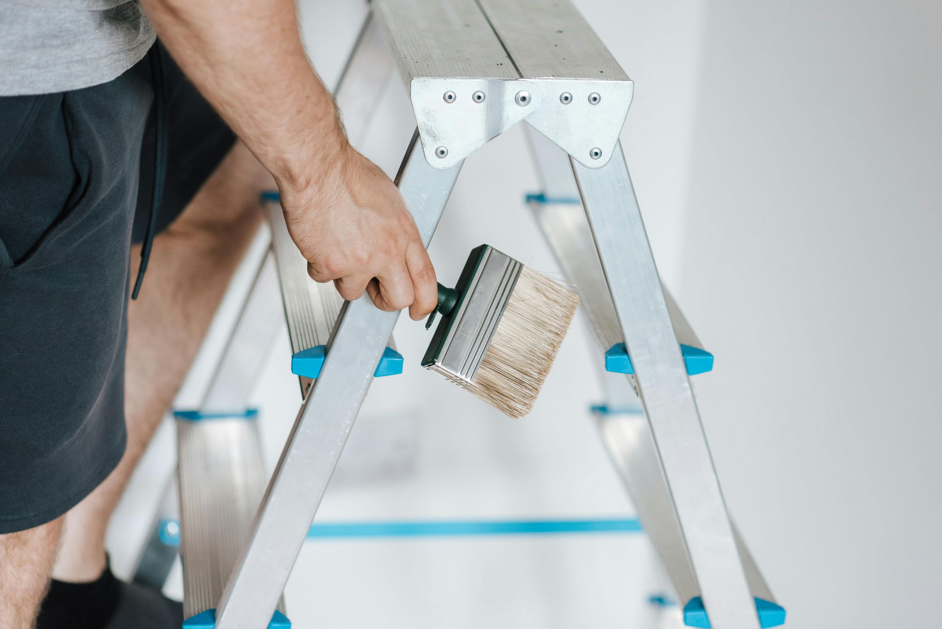 A man is sitting on a ladder holding a paint brush.