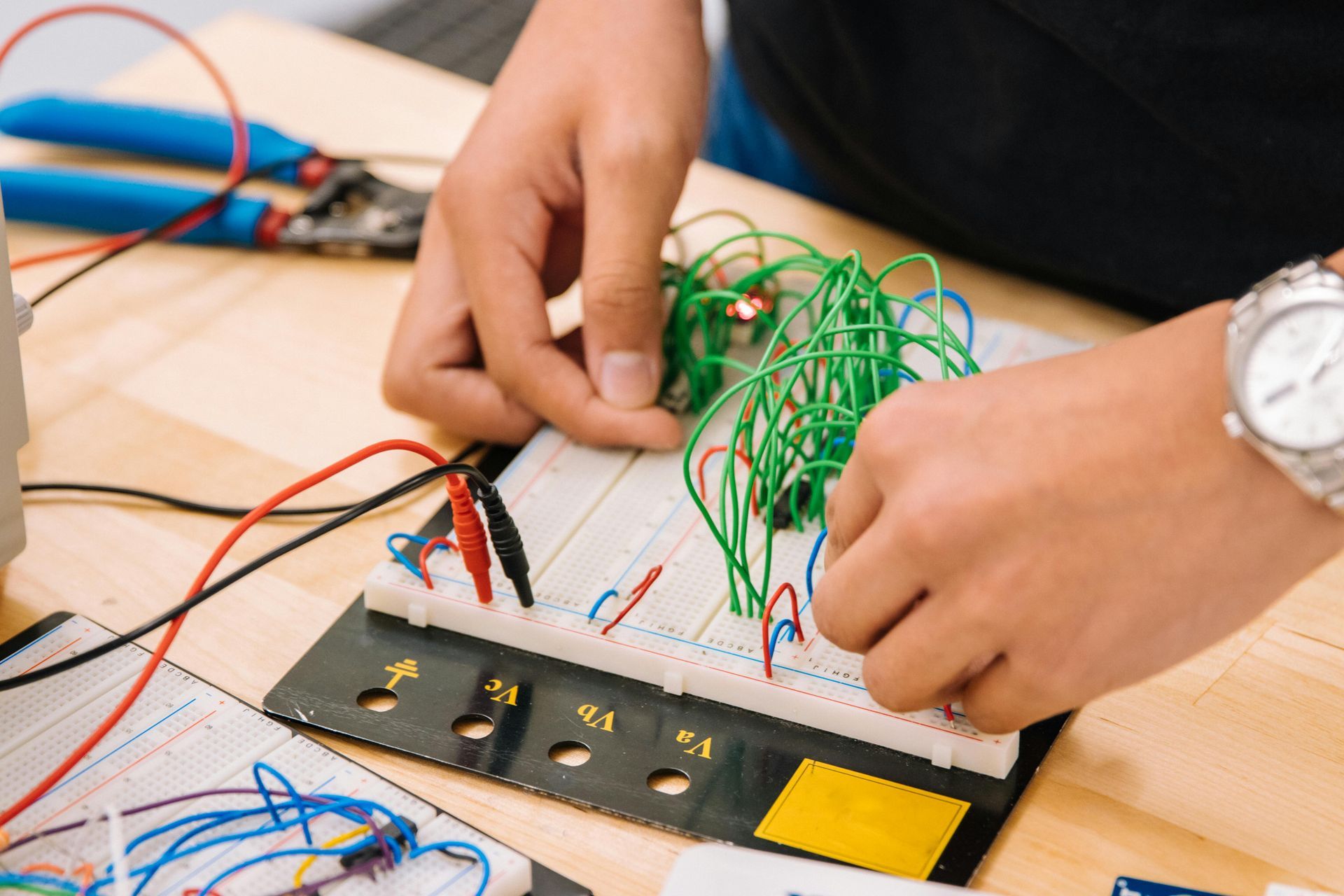 A person is working on a breadboard with wires and a watch on their wrist.