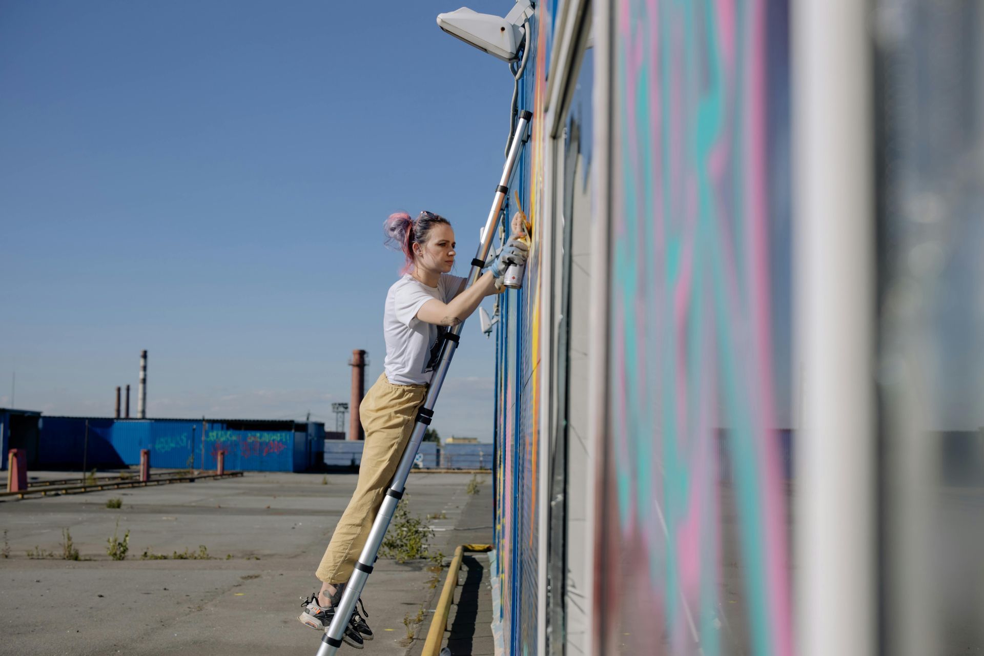 A woman is standing on a ladder painting a wall.