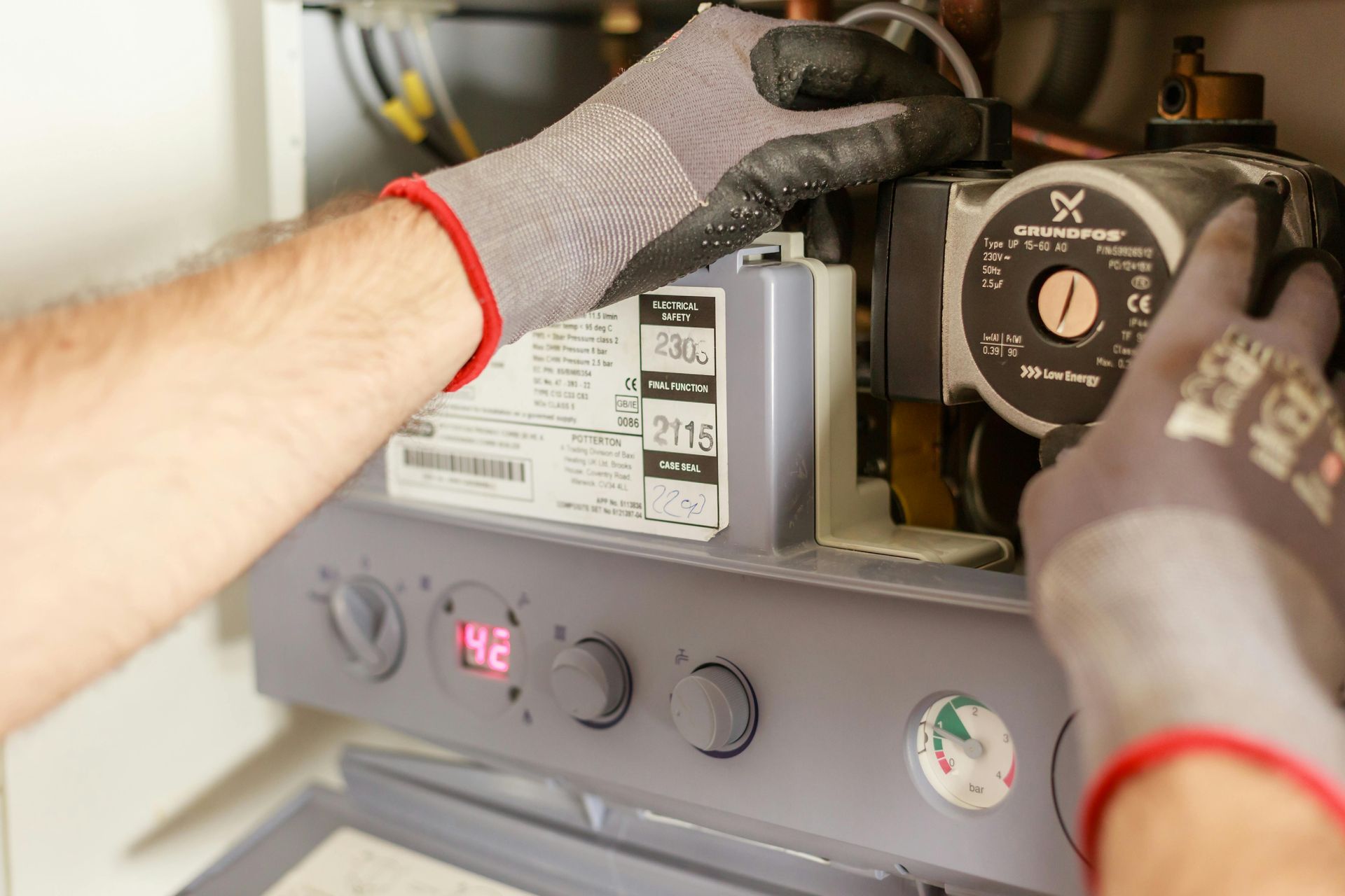 A man wearing gloves is working on a boiler.