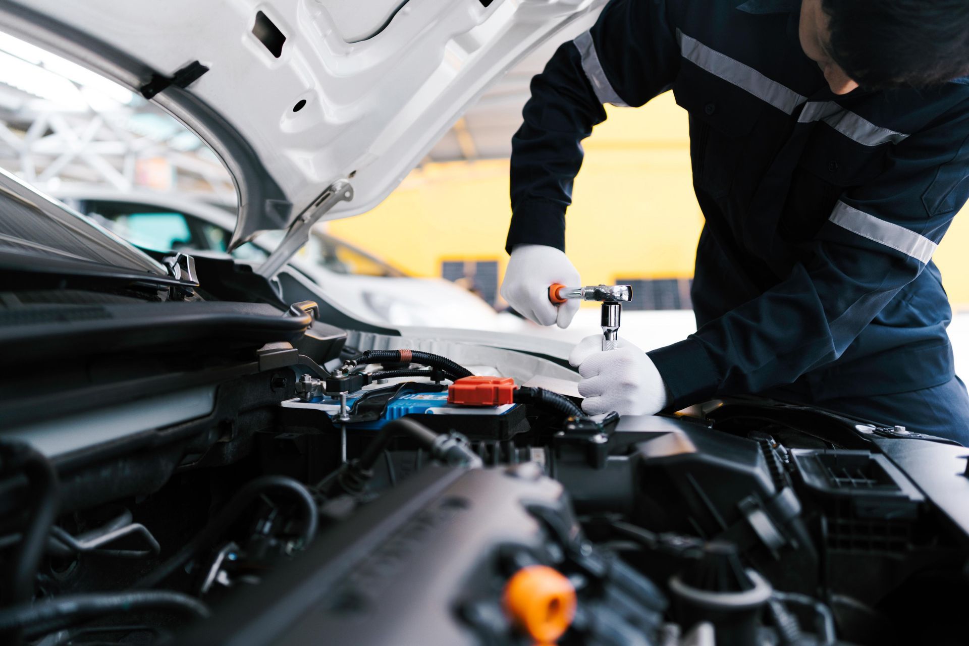 Mechanic using a wrench on a car engine with the hood open; indoor setting.