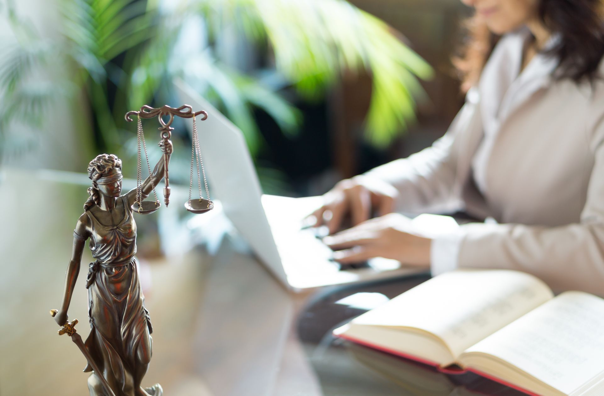 A woman is typing on a laptop next to a statue of justice.