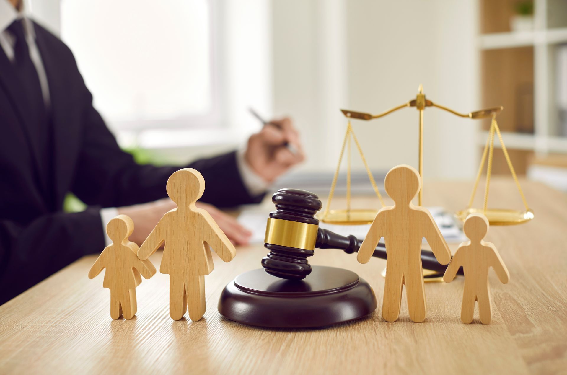 A wooden family is sitting on a wooden table next to a judge 's gavel and scales of justice.