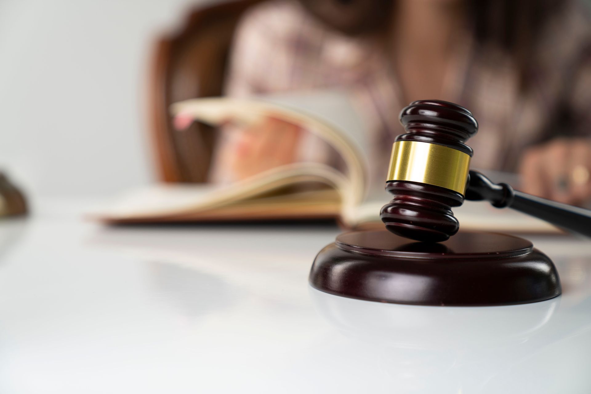 A judge 's gavel is sitting on a table in front of a woman reading a book.