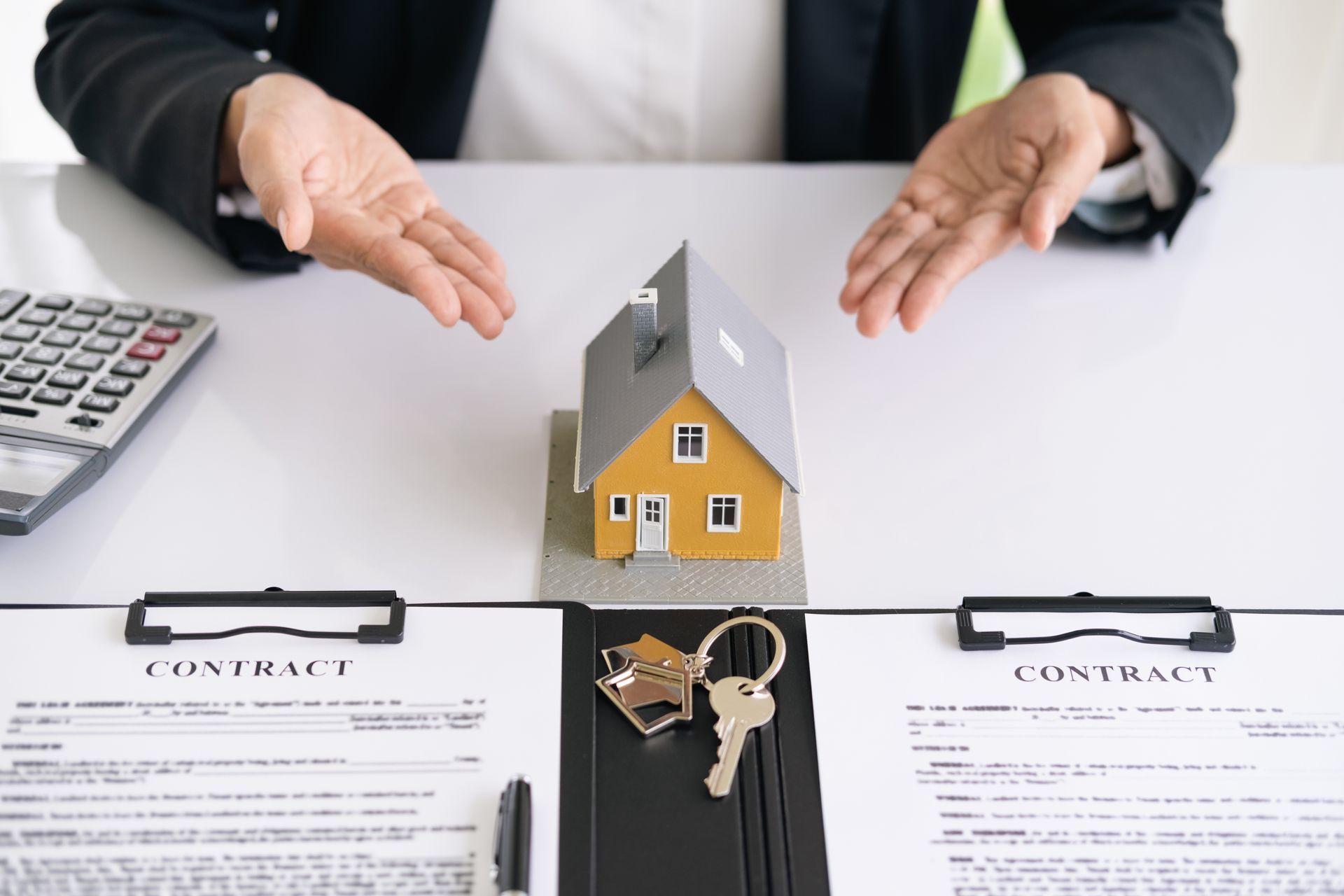 A man is sitting at a desk with a model house and keys.