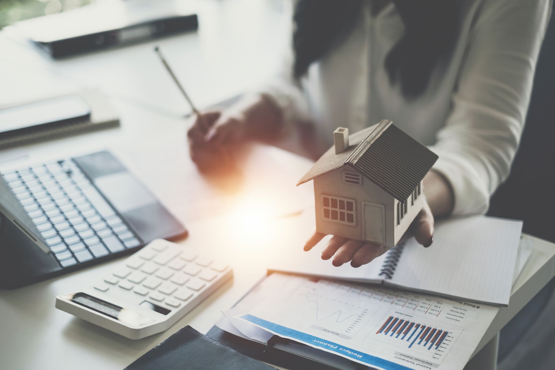 A woman is holding a model house in her hand while sitting at a desk.