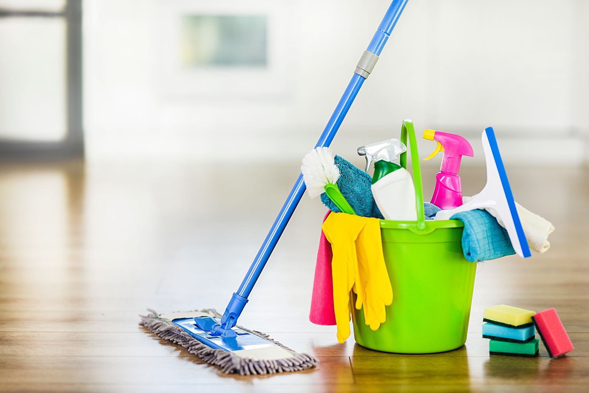 Mop leaning on a hardwood floor, next to a green bucket filled with cleaning supplies.
