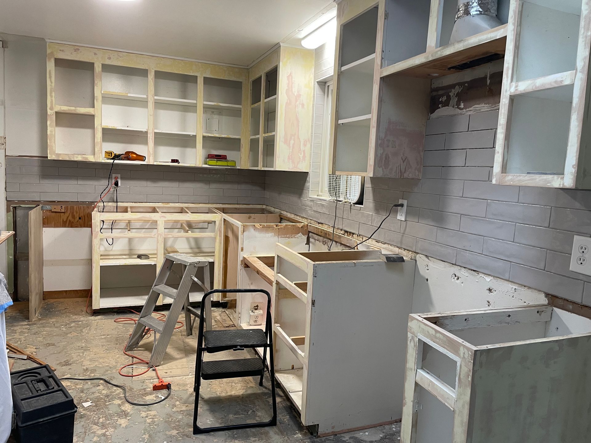 Kitchen under renovation, cabinets and brick backsplash exposed, tools scattered.