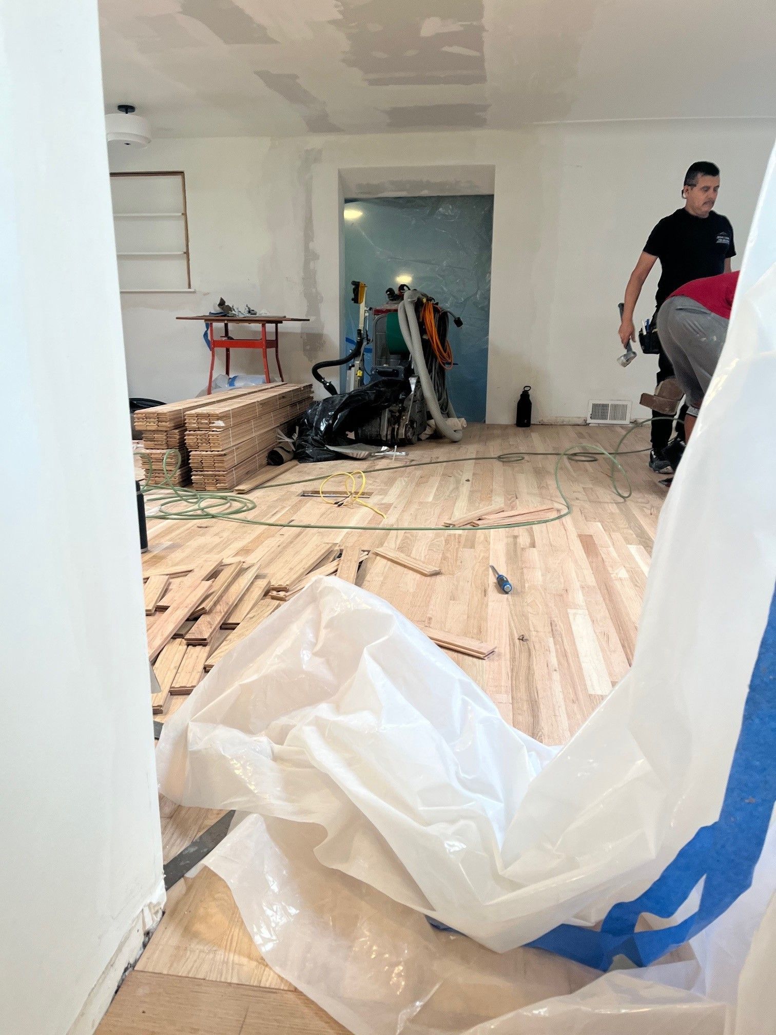 Room under renovation with exposed wood flooring, construction materials, and a worker.