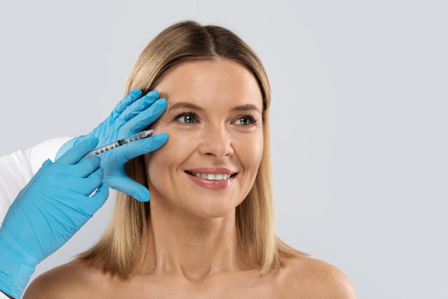 A woman is smiling while getting a botox injection in her face.