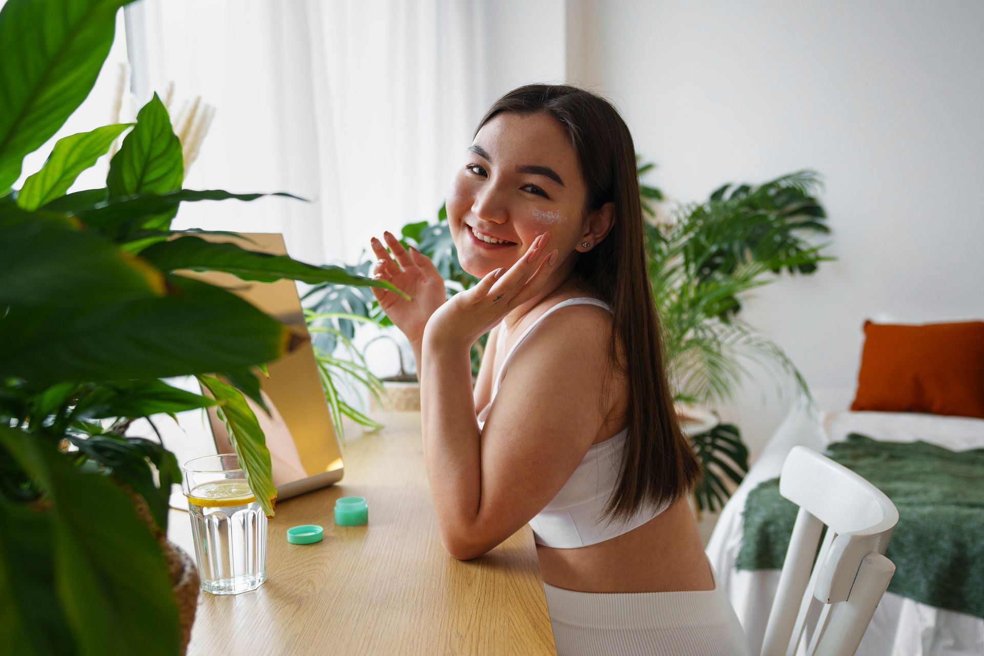 A woman in a white bra is sitting at a table with her hand on her face.