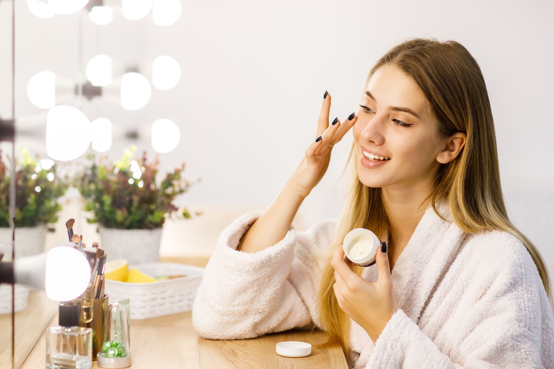 A woman is applying cream to her face in front of a mirror.