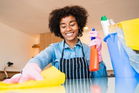 A woman is cleaning a table with a sponge and spray bottle.