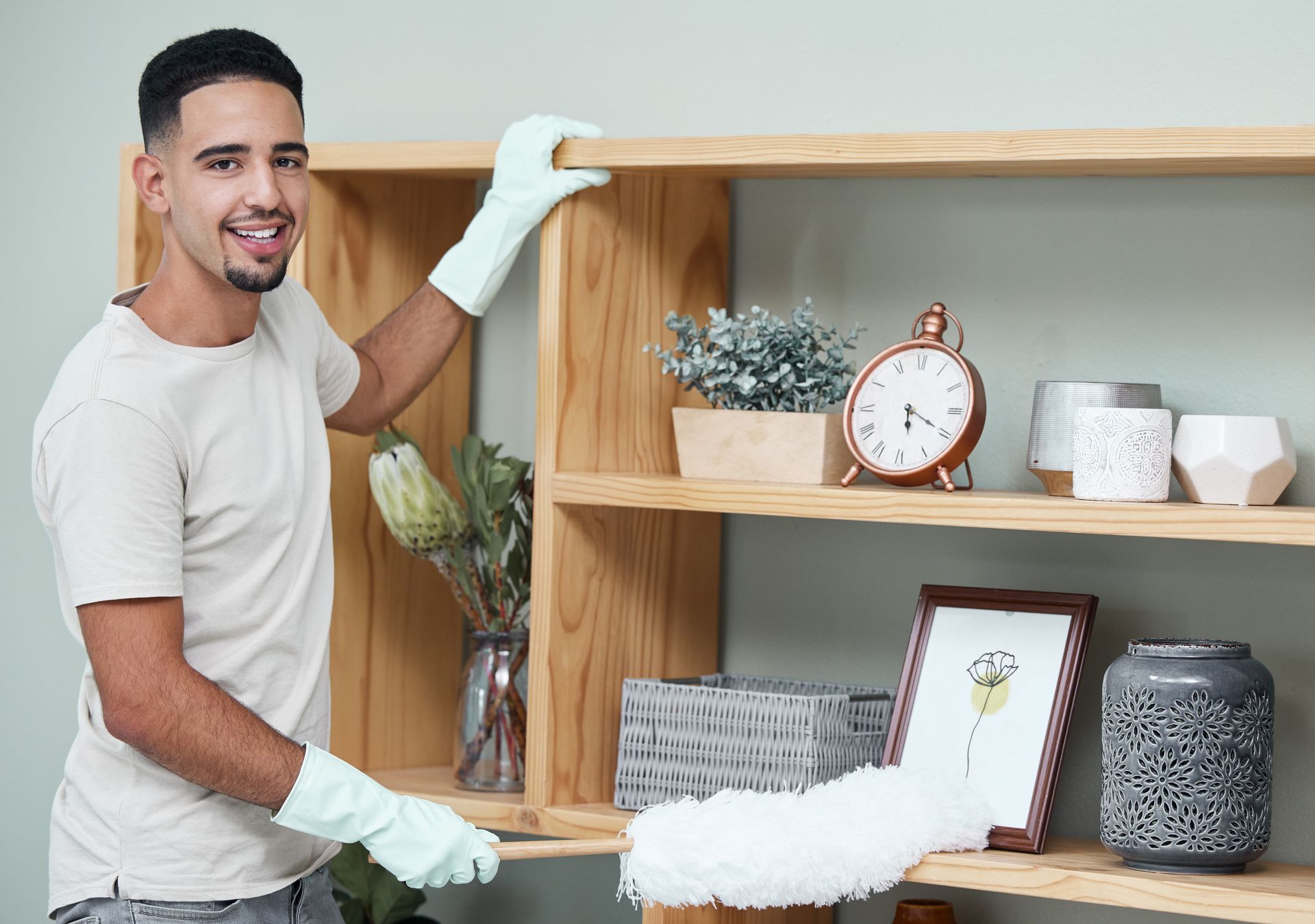 A man is cleaning a wooden shelf in a living room.