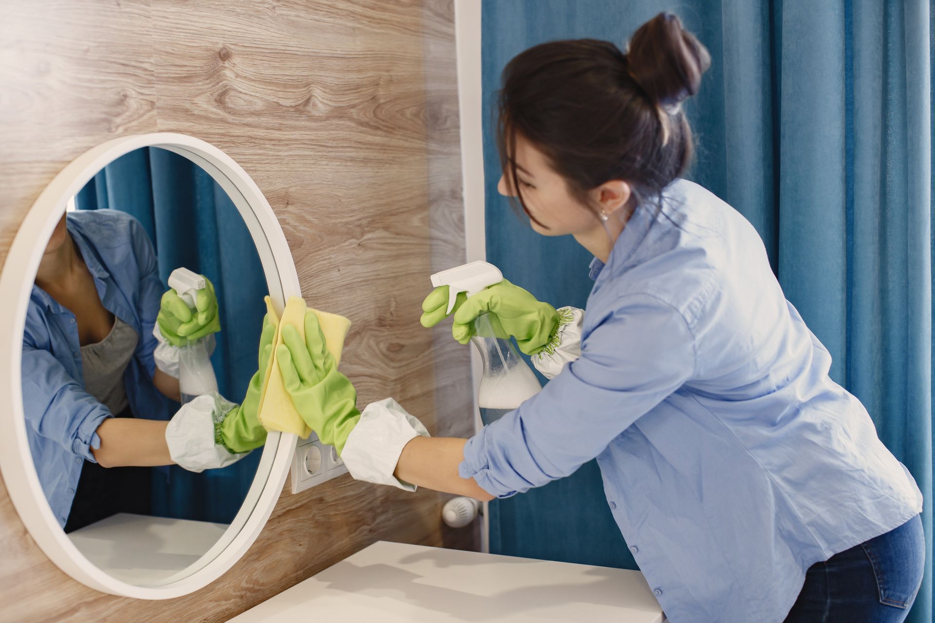 A woman is cleaning a mirror in a bathroom.