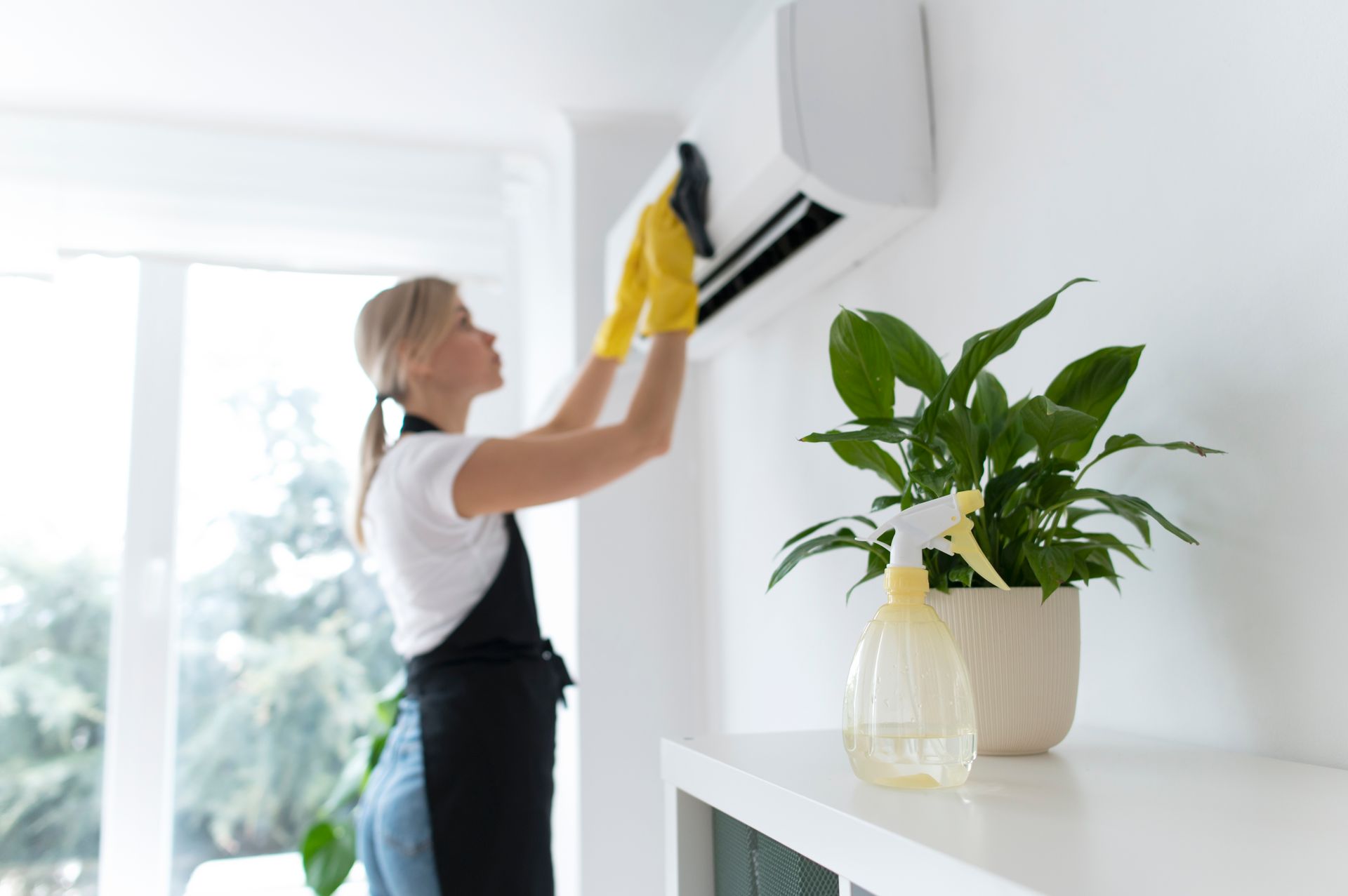 A woman is cleaning an air conditioner in a living room.