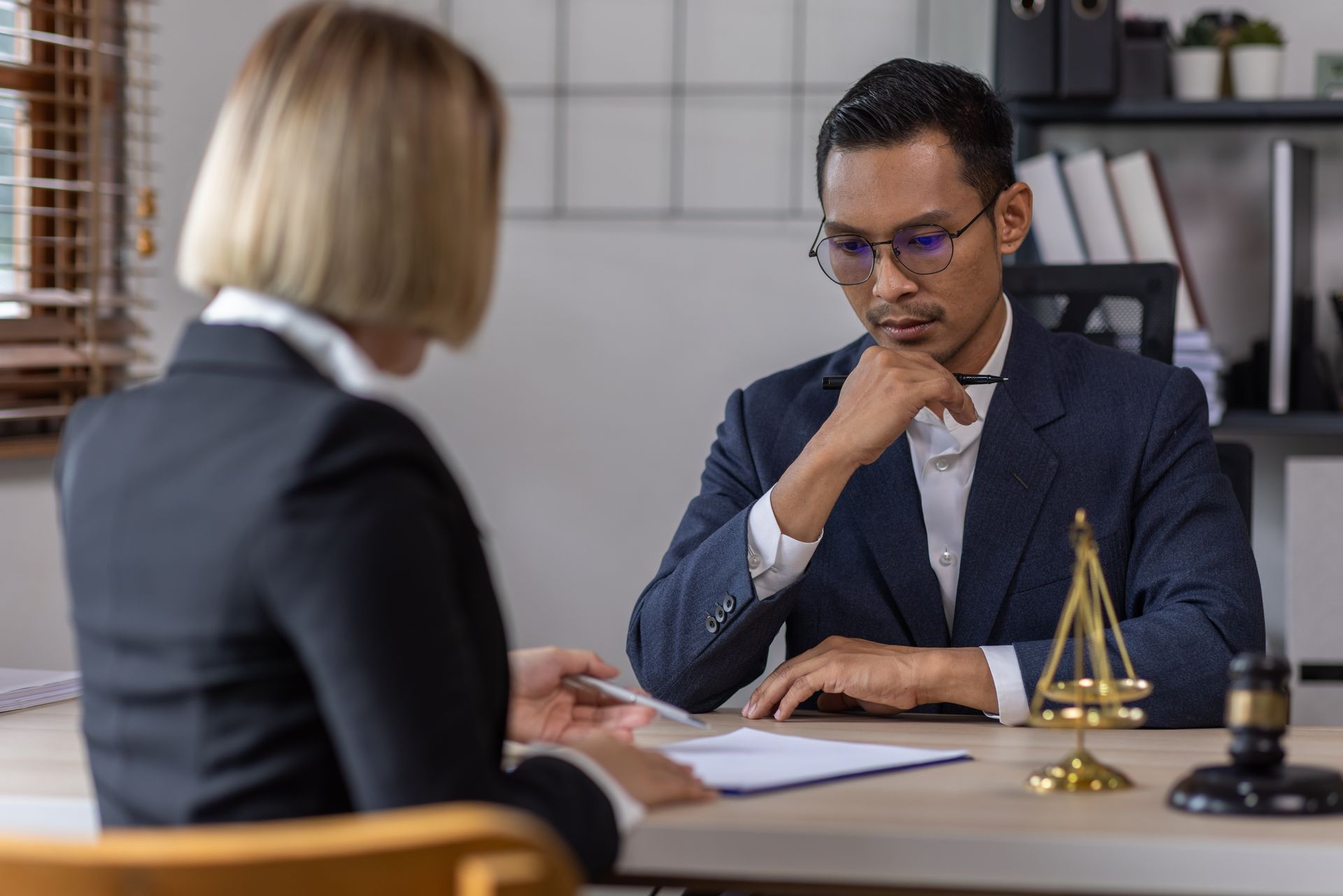 A lawyer and client sitting at a desk during a consultation, with a small gold scale of justice and a gavel on the table.