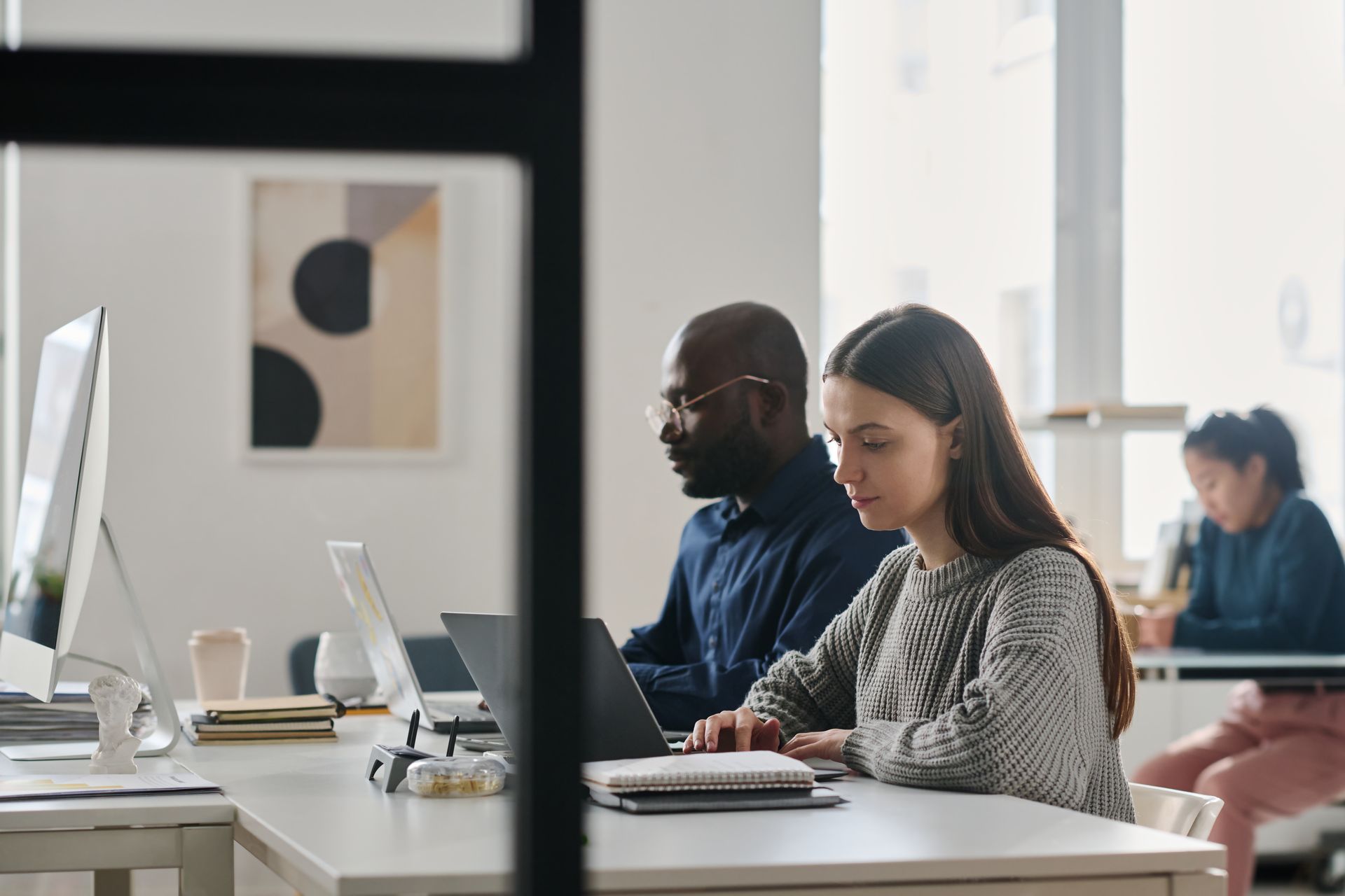 Three people working on laptops at desks in a modern office space.