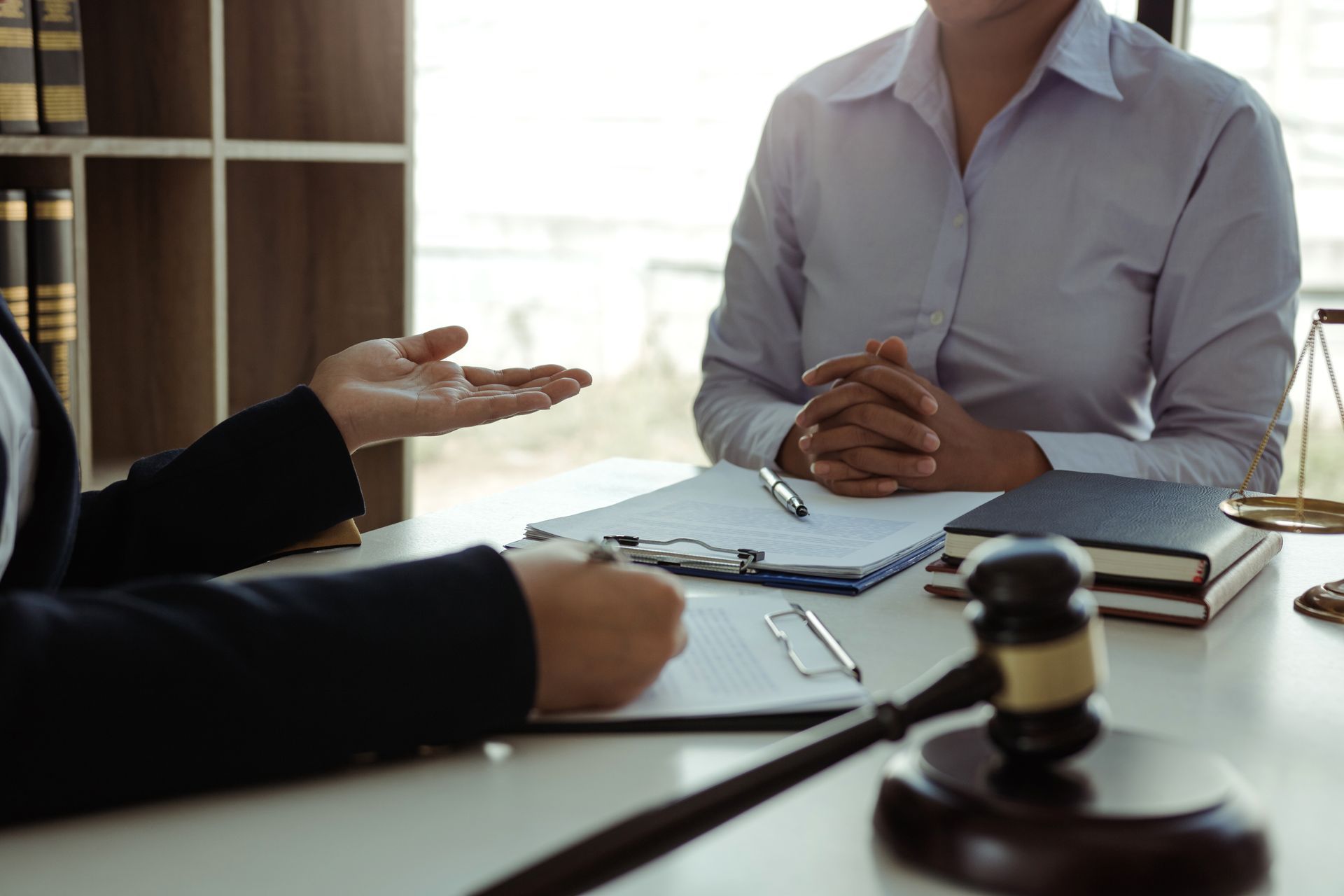 Two professionals sit at a desk with a gavel and legal documents, engaged in a discussion in a law office setting.